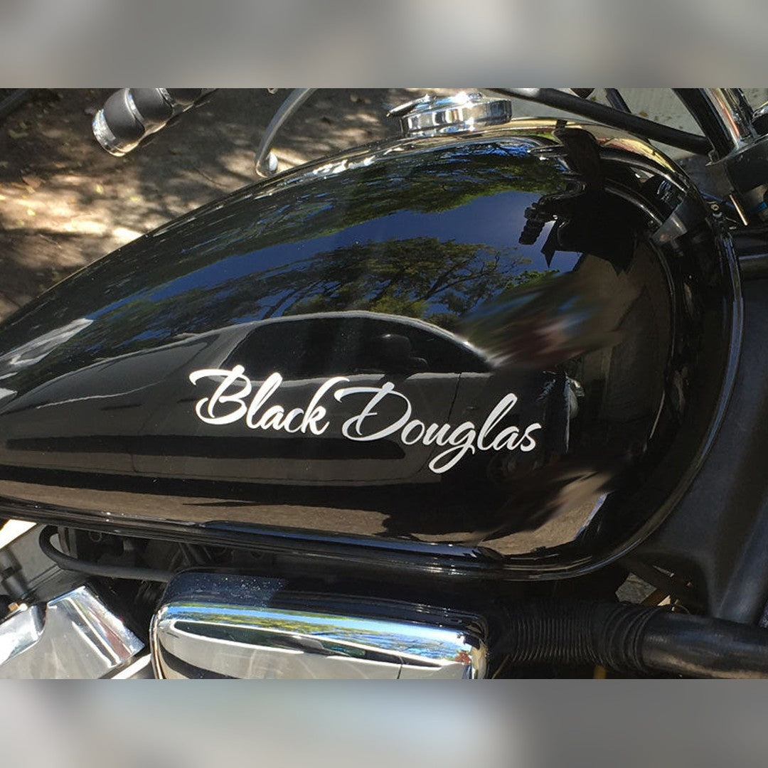 Custom name decal – white script lettering Black Douglas on the glossy black fuel tank of a motorcycle