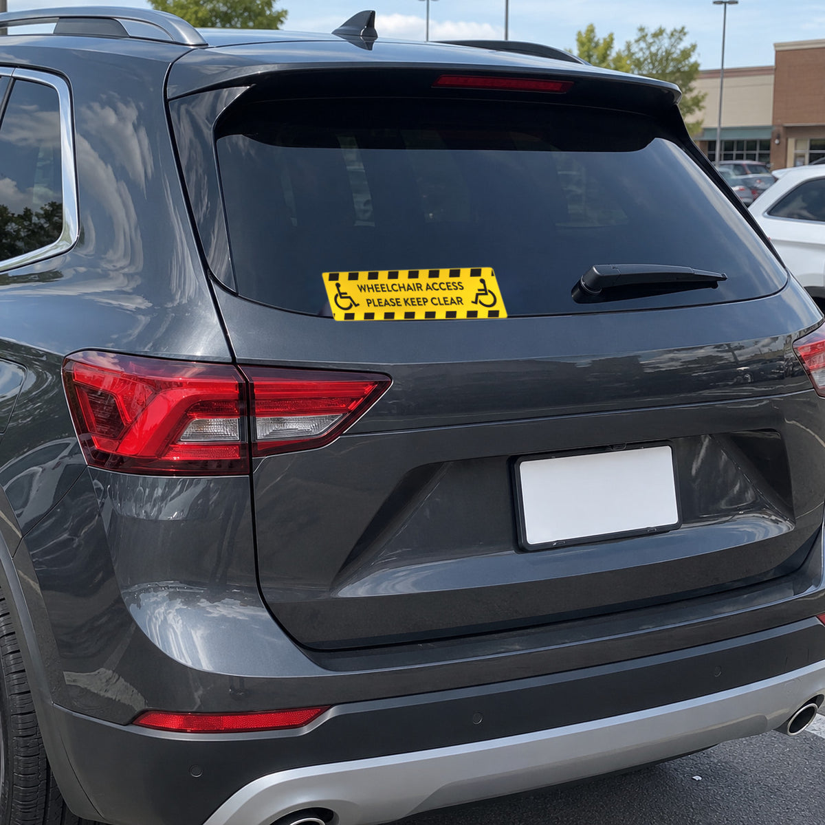 Option 1 yellow wheelchair access decal with black hazard stripes and two wheelchair symbols, WHEELCHAIR ACCESS, PLEASE KEEP CLEAR, applied to the rear window of a dark SUV.