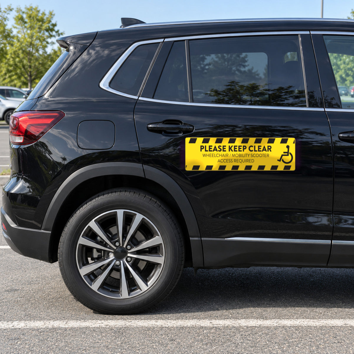 Option 2 yellow wheelchair access decal with black hazard stripes and a wheelchair symbol, PLEASE KEEP CLEAR, WHEELCHAIR / MOBILITY SCOOTER ACCESS REQUIRED, on the rear passenger door of a black SUV.