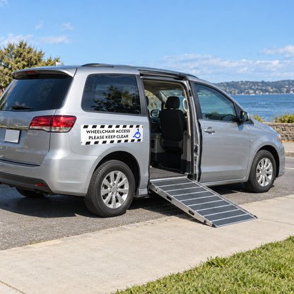 Option 3 white wheelchair access decal with black hazard stripes and a blue wheelchair symbol, reading WHEELCHAIR ACCESS, PLEASE KEEP CLEAR, beside the lowered side ramp of a silver minivan.