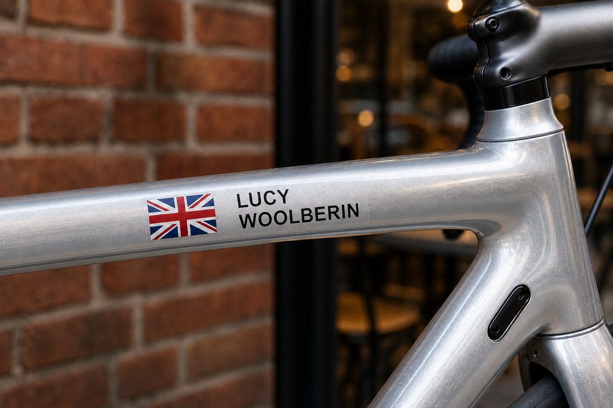 Custom flag and name sticker in block capitals with black lettering on a silver bicycle top tube, with Union Jack flag